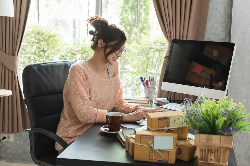 A young woman working at her home office desk perpendicular to the window for natural light.